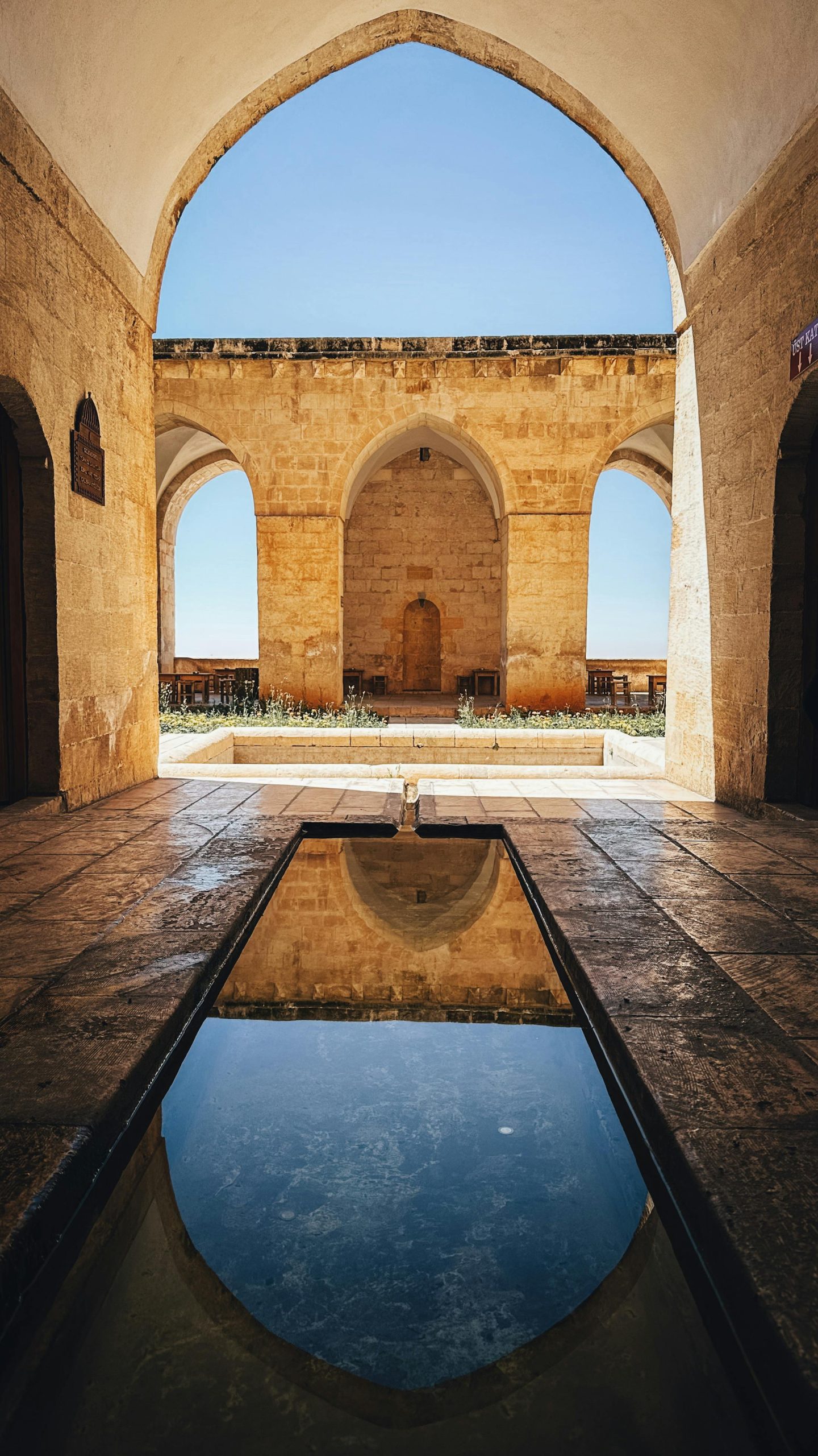 A serene courtyard with reflection pool and iconic arches in Mardin, Türkiye's historic architecture.